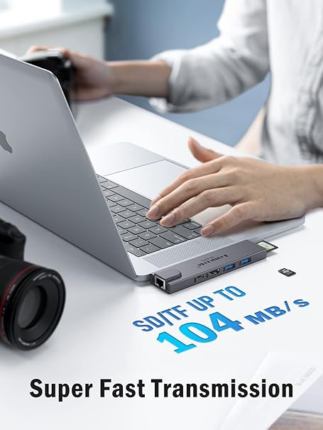 Person using a laptop with an external USB hub, camera on the side, and text 'Super Fast Transmission' and 'SD/TF UP TO 104 MB/s'.
