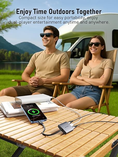 Two people sitting outdoors with a table displaying electronic devices, surrounded by nature.