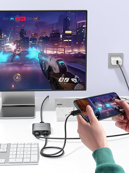 Person using a smartphone with a gaming app, connected to a computer monitor displaying a game.