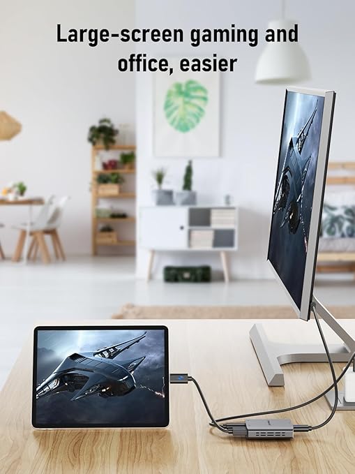 Two monitors displaying a spaceship image on a desk in a room with a white wall and plants.
