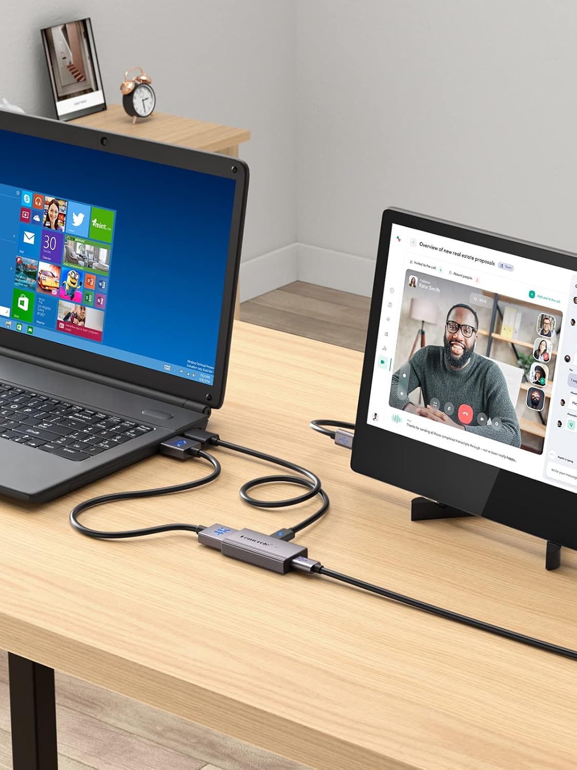 Laptop with screen extension device on a desk, connected to a monitor displaying a video call.